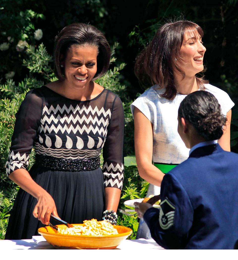 Michelle Obama and Samantha Cameron serve food to military families in 2011. Michelle wears a black and white dress.
