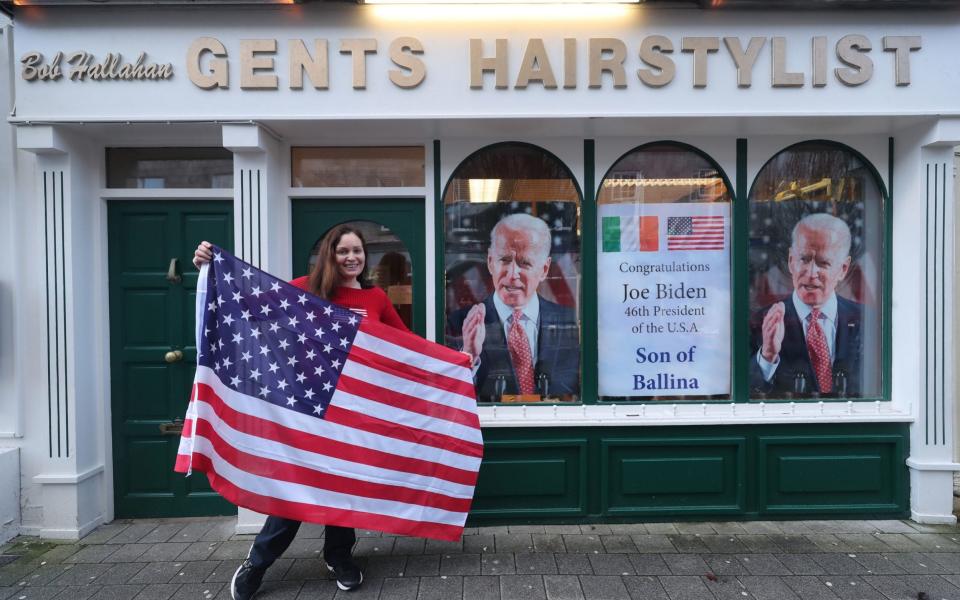 Catherine Hallahan prepares to hang an American flag inside her family's hairdressers in Ballina, Co Mayo to mark Mr. Biden's inauguration - Niall Carson /PA