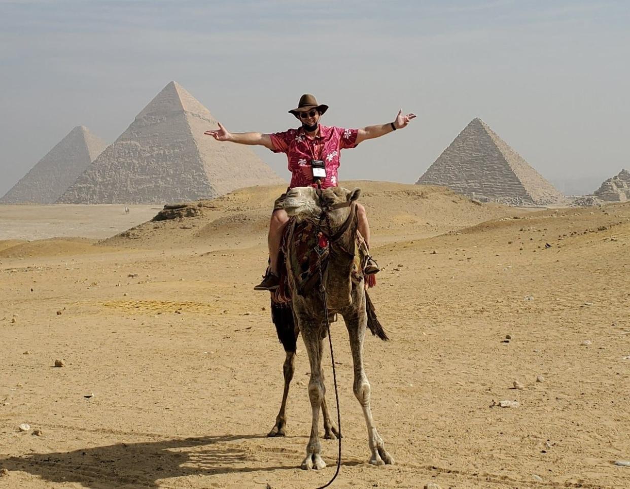 David Wahr is shown riding a camel. The Pyramids at Giza are in the background. Wahr's Feb. 10 presentation is Petersburg will include stories of his travels by camel.