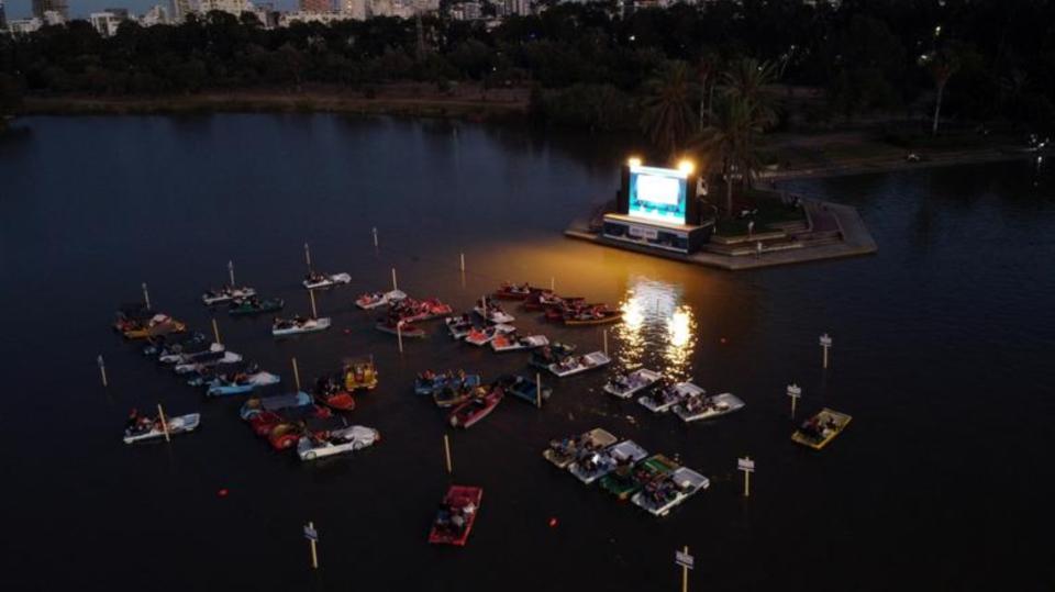 Varias personas asisten desde unos botes a la proyección de una película en un cine flotante instalado en el parque HaYarkon de Tel Aviv. (Foto: Ammar Award / Reuters).