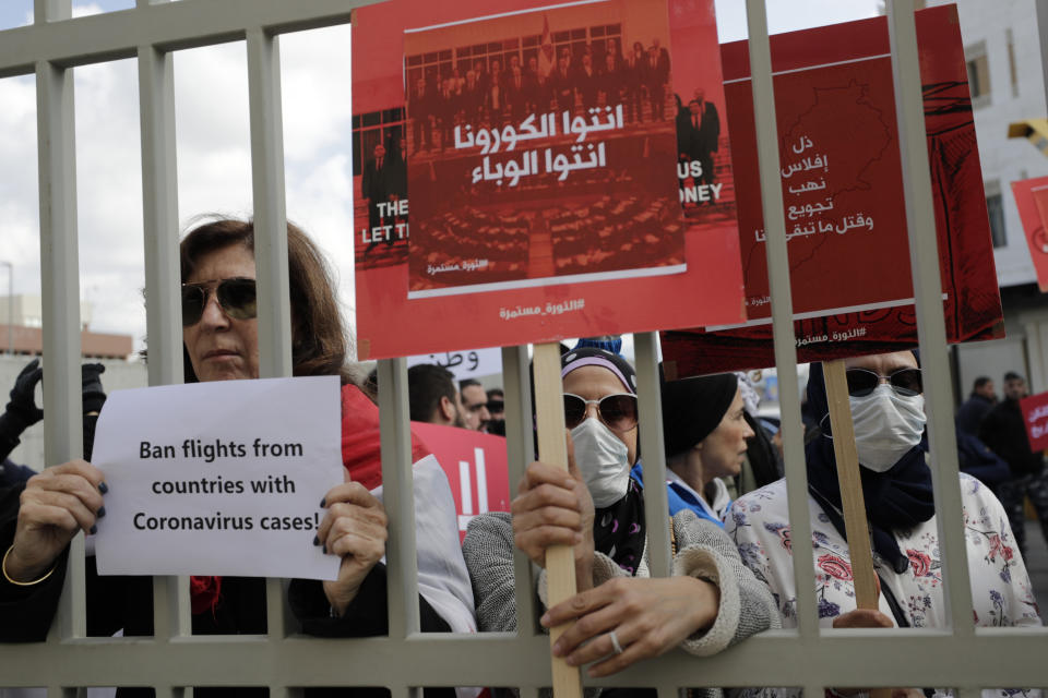 Anti-government protesters hold up banners in Arabic that read, "You are the coronavirus, you are the epidemic, (center) and Humiliation, bankruptcy, looting, starving and killing the rest of us, (right)," during ongoing protests against the Lebanese government in front of the Lebanese Ministry of Health, in Beirut, Lebanon, Wednesday, Feb. 26, 2020. (AP Photo/Hassan Ammar)