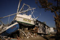 The "Night Wind" lies grounded against the second story of an apartment building, now missing its first story,on San Carlos Island in Fort Myers Beach, Fla., Friday, Oct. 7, 2022. Boat crew Shawn Shelton and Doug Fundak, along with Shelton's dog Lucky, rode the storm out on "Night Wind," as surge waters and wind carried it onshore and then into the apartment building. After the storm, many in the local shrimp industry find themselves not only out of work, but also homeless, with most of the boats where they lived aboard left stranded on dry ground or heavily damaged.(AP Photo/Rebecca Blackwell)