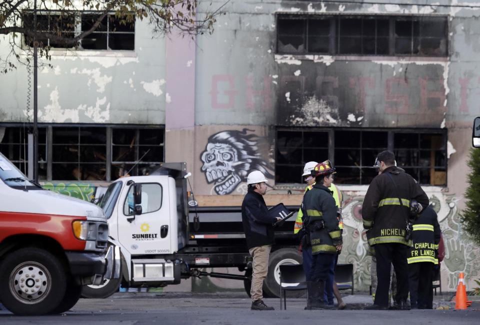 FILE - In this Monday, Dec. 5, 2016, file photo, emergency crews work in front of the site of a massive warehouse fire in Oakland, Calif. Micah Allison, the wife of the founder of a ramshackle Oakland artists' colony where dozens of people burned to death in a fire last month says she's sorry about what happened but is angry about what she called "pretty terrible" treatment by the media and ex-neighbors. (AP Photo/Marcio Jose Sanchez, File)