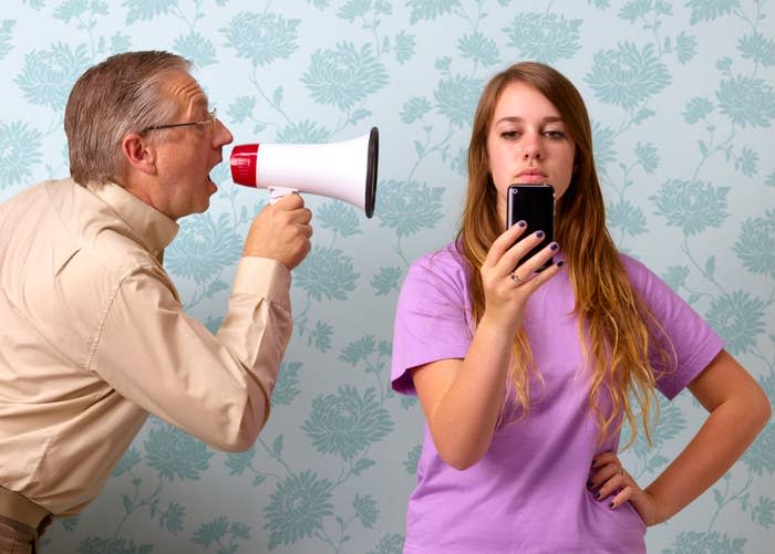 An older man yelling at a young girl through a megaphone while she looks at her cellphone