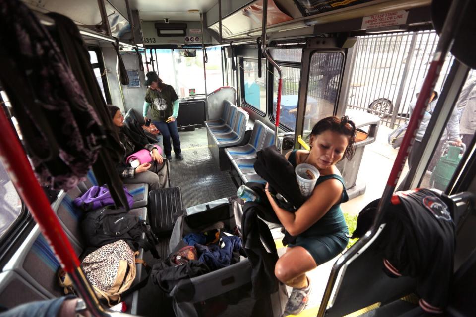 A woman, arms laden with belongings, boards a bus