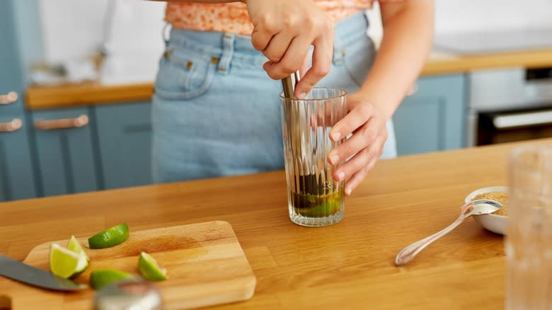 Hands muddling citrus fruit in a glass