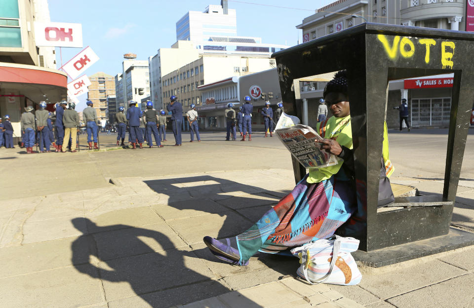 A newspaper vendor reads a copy of a daily paper as police block a main road ahead of a planned protest in Harare, Friday, Aug. 16, 2019. Zimbabwe's police patrolled the streets of the capital Friday morning while many residents stayed home fearing violence from an anti-government demonstration planned by the opposition. (AP Photo/Tsvangirayi Mukwazhi)