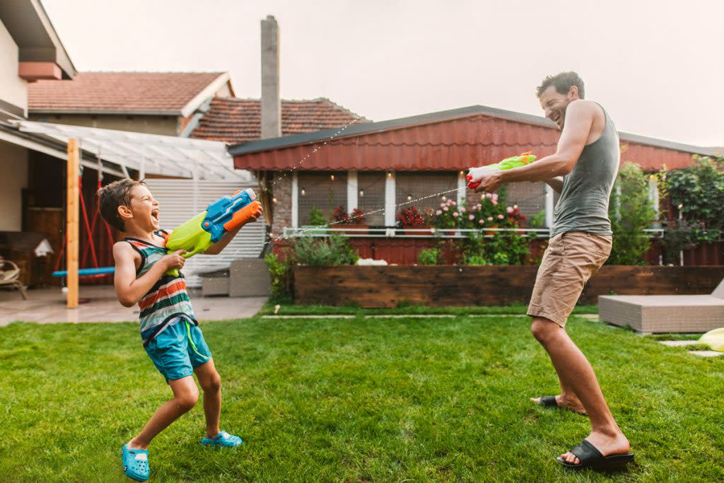 A son and father have a water gun fight in their backyard.