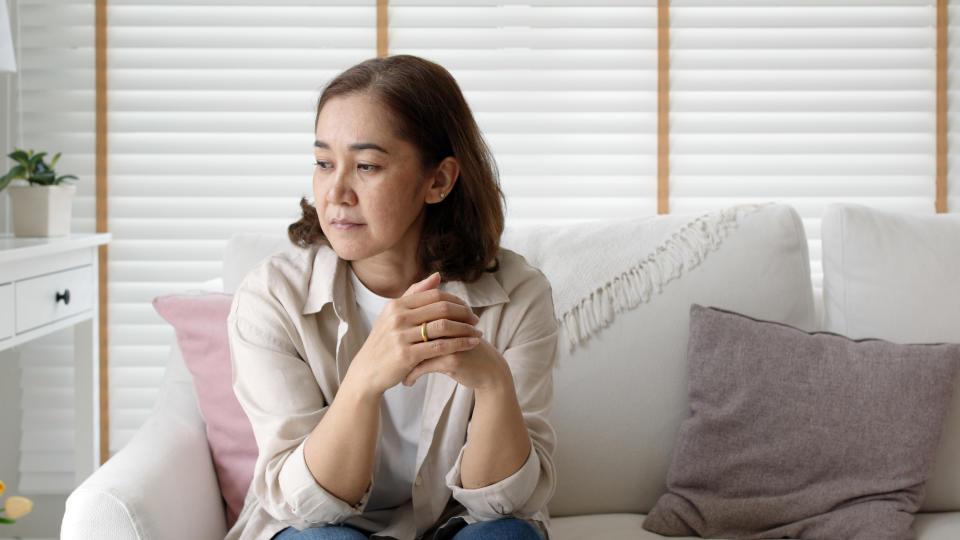 a middle-aged adult sitting on the couch and looking down