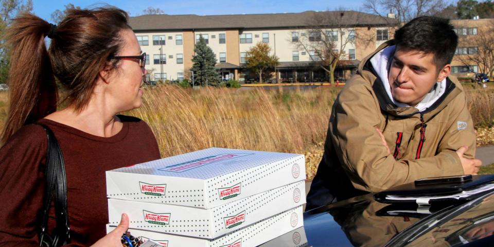 In this Saturday, Oct. 26, 2019 photo, Catherine Newton, left, buys three boxes of Krispy Kreme doughnuts from Jayson Gonzalez in Little Canada, Minn. Gonzalez, a Minnesota college student, says Krispy Kreme has told him to stop making doughnut runs to Iowa. Gonzalez told the Pioneer Press he was told his sales created a liability for the North Carolina-based company.  (Deanna Weniger/Pioneer Press via AP)