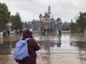 A visitor stands in the rain at Disneyland in Anaheim, Calif., Friday, March 13, 2020. Disneyland is closing its doors for the rest of the month, shuttering one of California's best-known attractions as the state hurries to stop the spread of the coronavirus. (AP Photo/Amy Taxin)