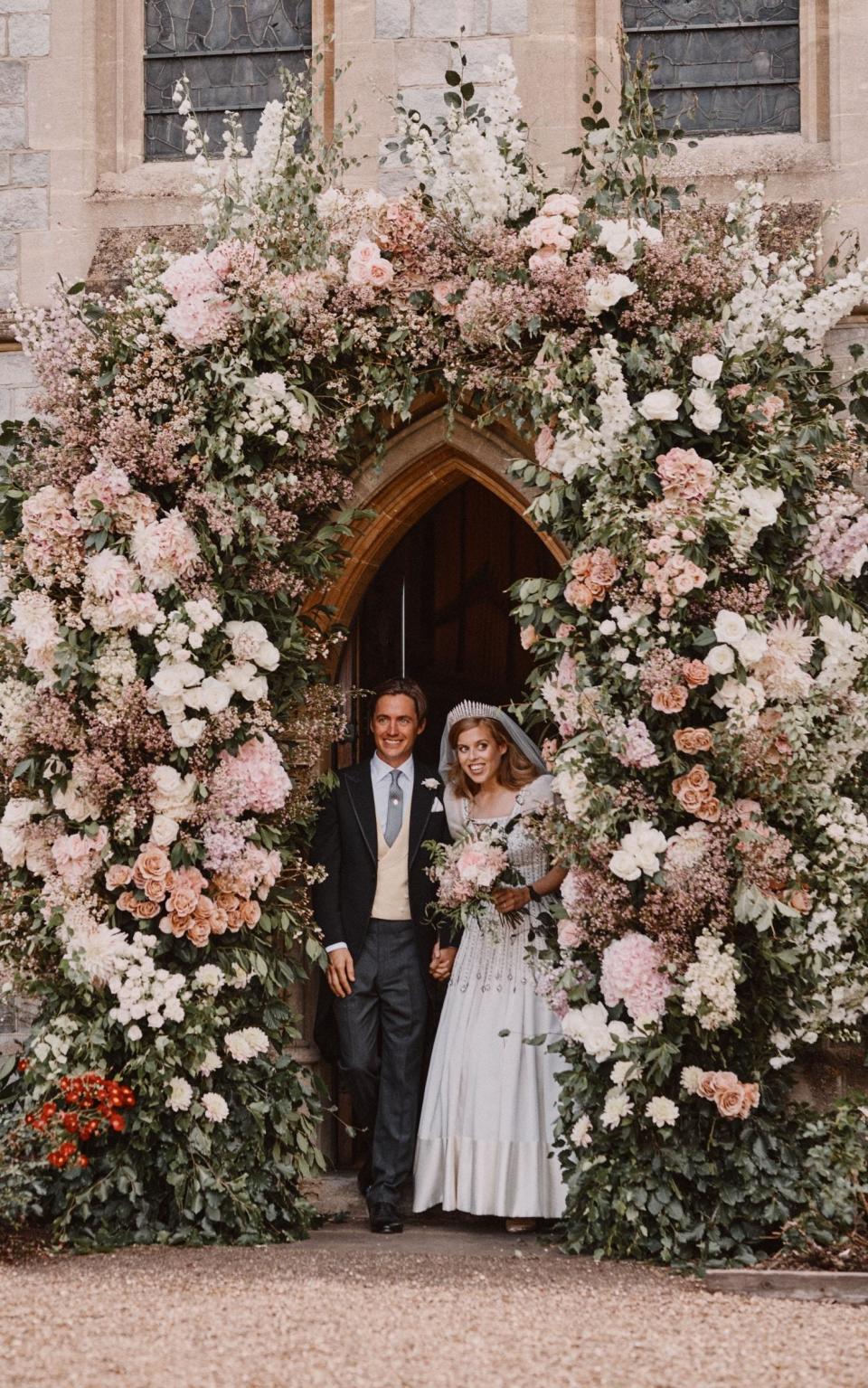 The happy couple emerging from a dramatic floral archway - Benjamin Wheeler /WPA Pool 