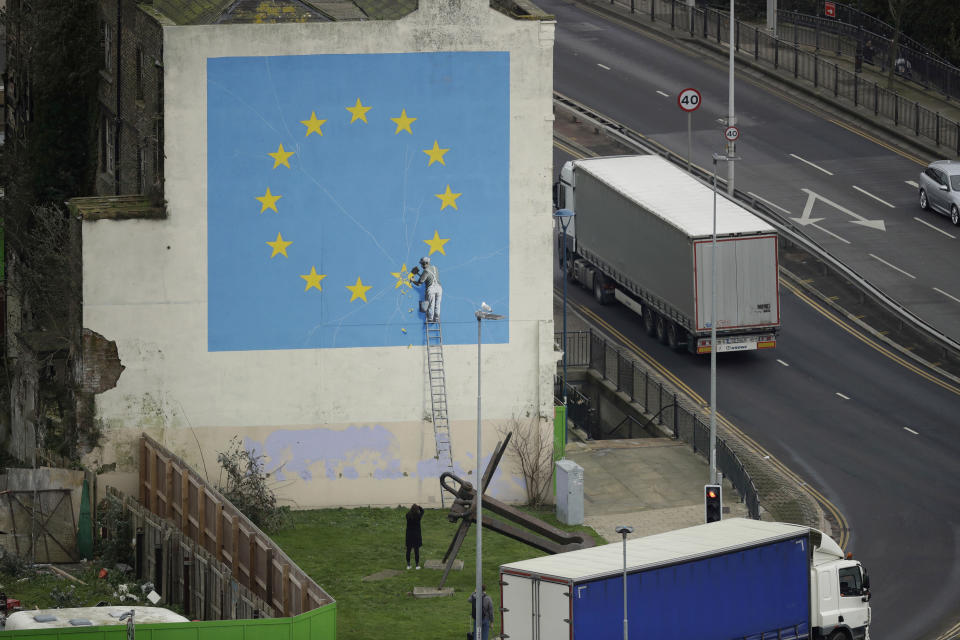 A woman takes a photograph of a mural by street artist Banksy showing a star being chiselled from the European flag in Dover, south east England, Monday, Jan. 7, 2019. Britain is testing how its motorway and ferry system would handle a no-deal Brexit by sending a stream of trucks from a regional airport to the port of Dover — even as some legislators try to pressure the government to rule out the scenario. (AP Photo/Matt Dunham)