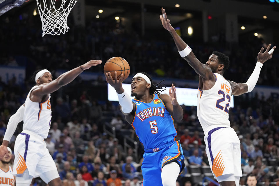 Oklahoma City Thunder guard Luguentz Dort (5) goes to the basket between Phoenix Suns forward Josh Okogie, left, and center Deandre Ayton (22) in the first half of an NBA basketball game Sunday, April 2, 2023, in Oklahoma City. (AP Photo/Sue Ogrocki)