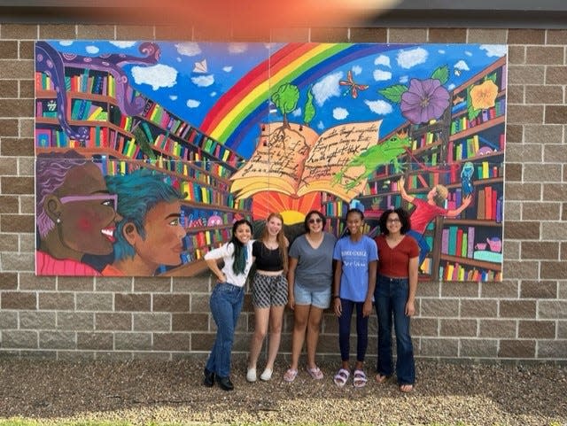 Youth artists Lauryn Essien, Gigi Goodvin, Malia Parker, and Catie Vest pose with the completed mural now on display at the North Liberty Library.