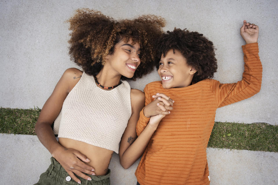 Woman and child lying on ground, smiling at each other, woman in polka dot top, child in orange shirt