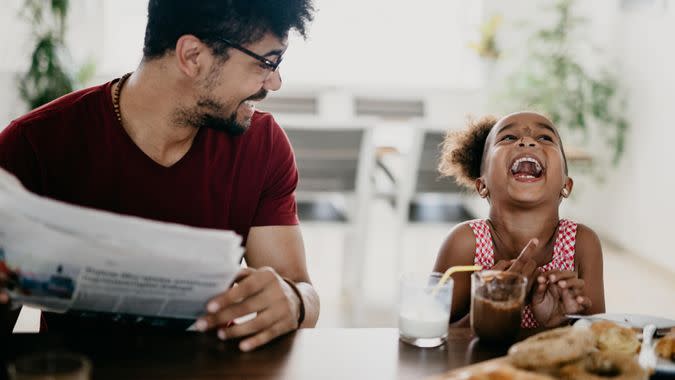 Little girl bursts into laugh while having breakfast with her father.