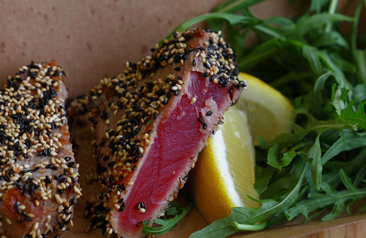 Close up street food brown carton box portion of lightly seared tuna steak with sesame seeds and arugula salad