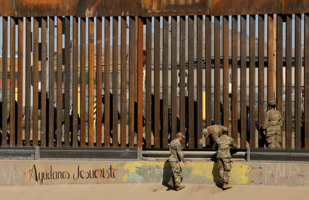 FILE PHOTO: U.S. soldiers walk next to the border fence between Mexico and the United States, as migrants are seen walking behind the fence, after crossing illegally into the U.S. to turn themselves in, in El Paso, Texas, U.S., in this picture taken from Ciudad Juarez, Mexico, April 3, 2019. The writing on the wall reads, "Help us Jesus Christ." REUTERS/Jose Luis Gonzalez/File Photo