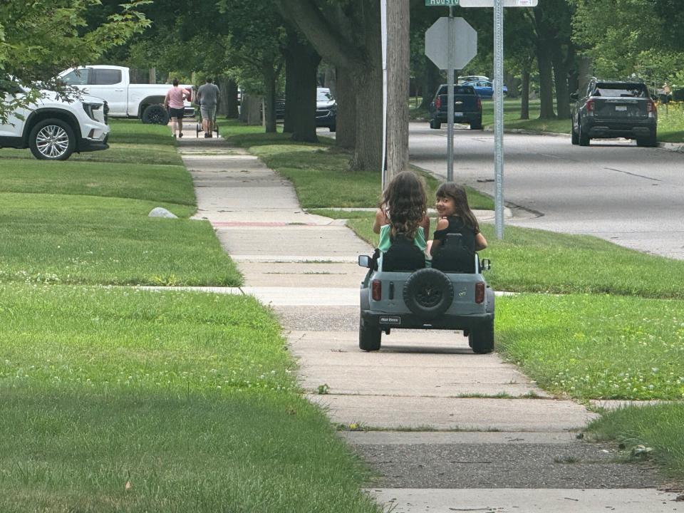 Tala Young, 9, drives her toy Ford Bronco while Kaya Young, 5, sits in the passenger seat looking back over her shoulder in Royal Oak, Mich., on June 26. They are the daughters of Jovina Young, director of charging services at Ford Motor Co.