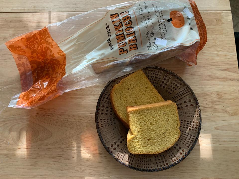 Open bag of Trader Joe's Pumpkin brioche alongside a plate with two slices on a wooden table