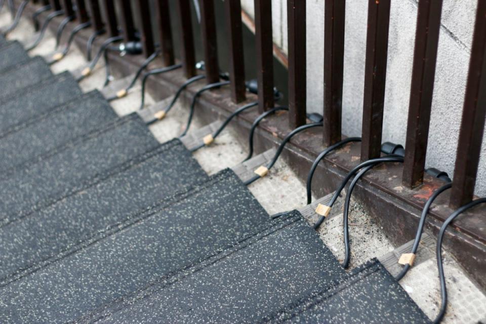 Snow melting mats hooked on to an iron railing on a tall outdoor stair.