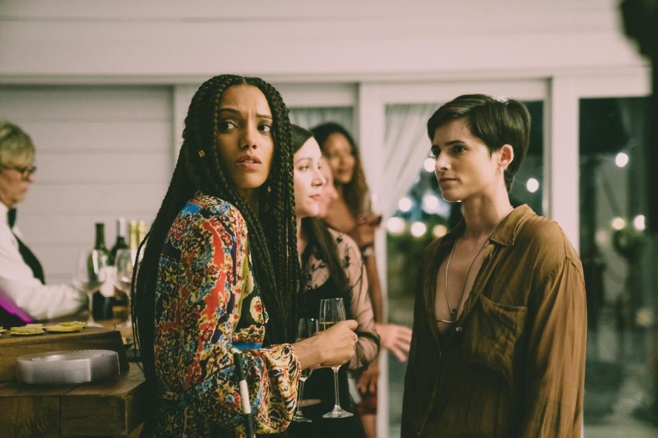 Kat Graham and Nina Kiri at a social event, holding glasses, engage with other attendees in the background