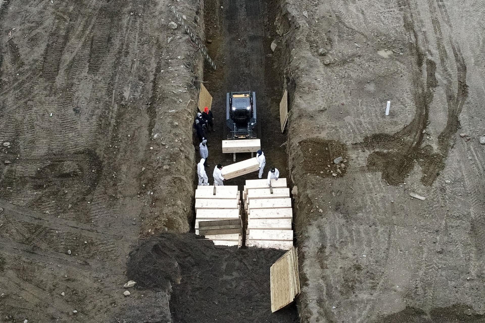 FILE - In this April 9, 2020, file photo, workers wearing personal protective equipment bury bodies in a trench on Hart Island in the Bronx borough of New York. As coronavirus rages out of control in other parts of the U.S., New York is offering an example after taming the nation’s deadliest outbreak this spring — but also trying to prepare in case another surge comes. (AP Photo/John Minchillo)