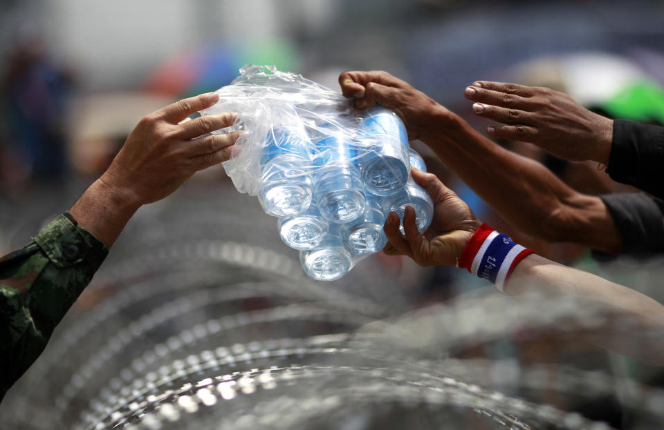 Thai anti-government protesters led by Suthep Thaugsuban, right, receive bottles of drinking water from a Thai soldier across the barbed wire during a rally outside the office of Permanent Secretary for Defense, a temporary office of Prime Minister Yingluck Shinawatra, on the outskirts of Bangkok, Thailand Wednesday, Feb. 19, 2014. Anti-government protesters surrounded Yingluck's temporary office in Bangkok's northern outskirts to demand her resignation a day after clashes with police. (AP Photo/Wason Wanichakorn)