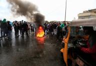 Iraqi demonstrators warm themselves as they block the highway during ongoing anti-government protests in Baghdad