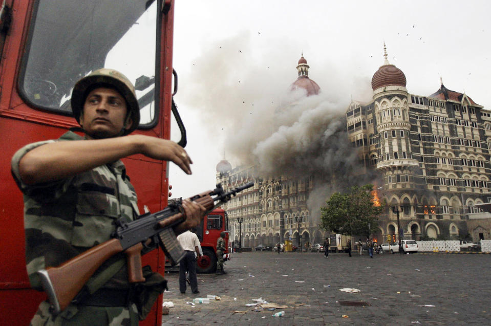 FILE- An Indian soldier takes cover as the Taj Mahal hotel burns during a gun battle between Indian military and militants inside the hotel in Mumbai, India, Nov. 29, 2008. The three days of terror in Mumbai carried out by the Pakistan-based militant group Lashkar-e-Taiba left 166 people dead. (AP Photo/David Guttenfelder, File)