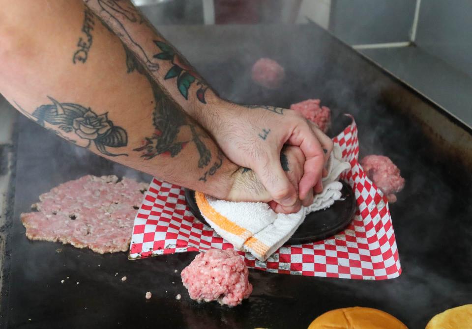 Chef Steffan Rost smashes the burger patties down on the grill as he prepares Smash Burgers at the Crispi food truck at Two Tides Brewing Company on West 41st Street.