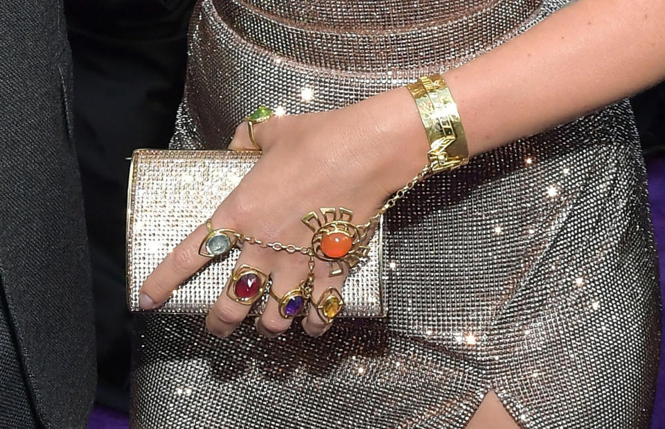 Close-up of a person's adorned hand with a sparkling clutch, gold bracelet, and colorful rings