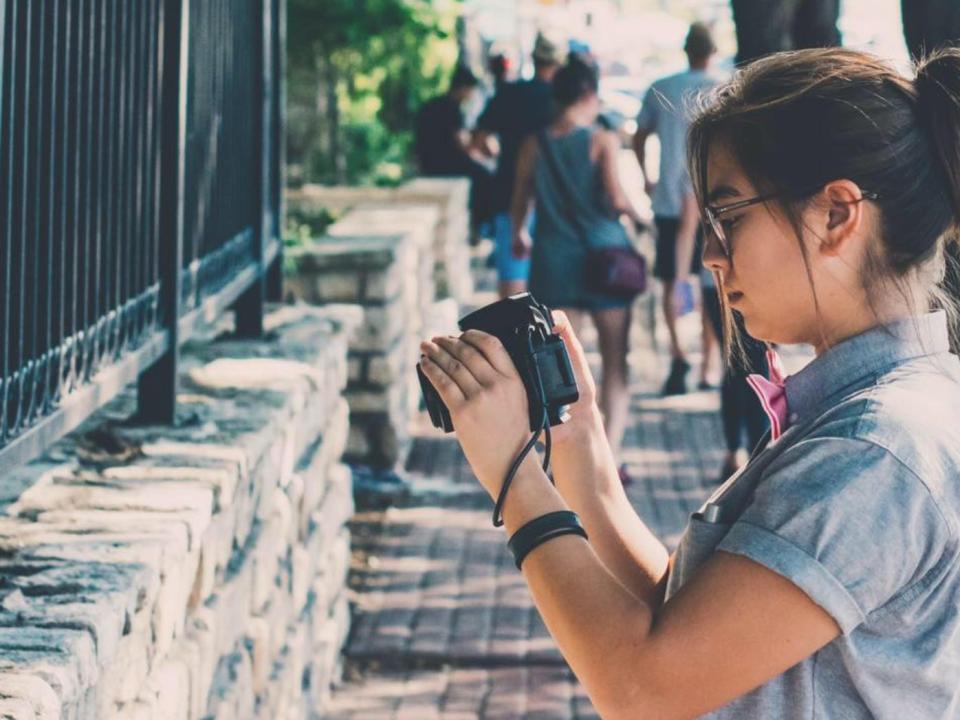The author takes a photo on the street in Austin Texas with trees and pedestrians behind her