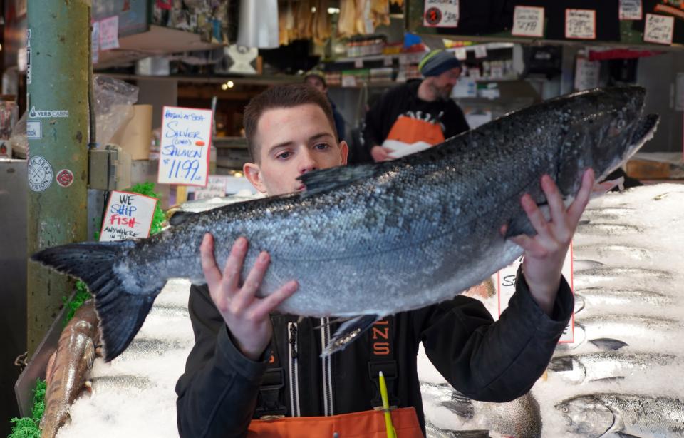 Fishmonger Nic Grimmer holds up a whole salmon offered for sale at the Pike Place Fish Market in Seattle on March 5, 2020.