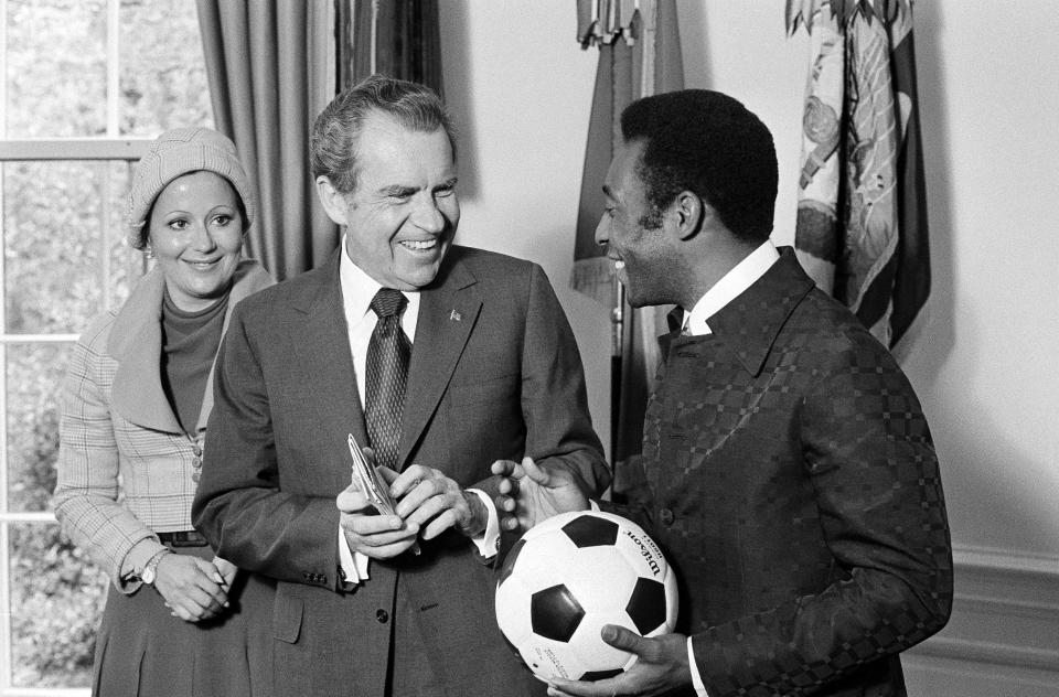 FILE - In this May 8, 1973 file photo, Brazil's soccer player Pele holds a ball he autographed for U.S. President Richard Nixon, who holds a 1957 newspaper clipping shown them together in Sao Paolo, Brazil, and Pele's wife Rosemeri dos Reis Cholbi looks on, at the chief executive's office in Washington, D.C. On Oct. 23, 2020, the three-time World Cup winner Pelé turns 80 without a proper celebration amid the COVID-19 pandemic as he quarantines in his mansion in the beachfront city of Guarujá, where he has lived since the start of the pandemic. (AP Photo/Henry Burroughs, File)