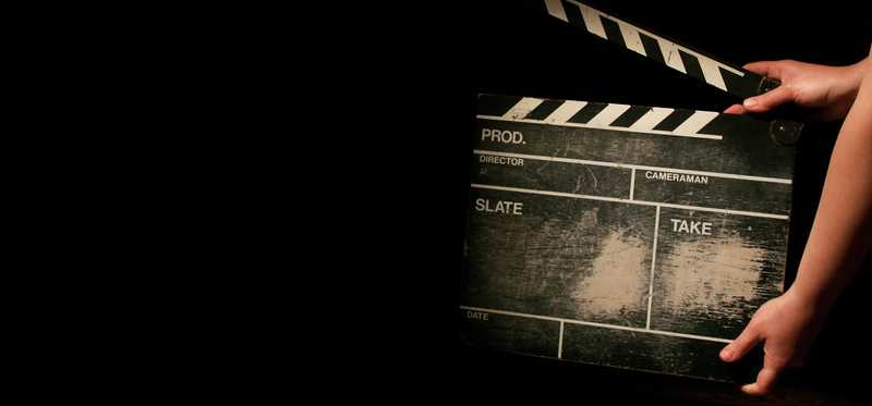 Movie clapperboard being held against a dark background.