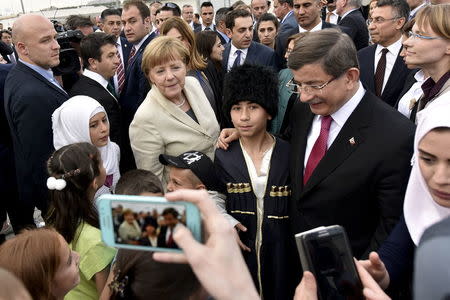 Turkish Prime Minister Ahmet Davutoglu and German Chancellor Angela Merkel pose for a picture with refugees in Nizip refugee camp near Gaziantep, Turkey, April 23, 2016. Bundesregierung/Steffen Kugler/Handout via REUTERS