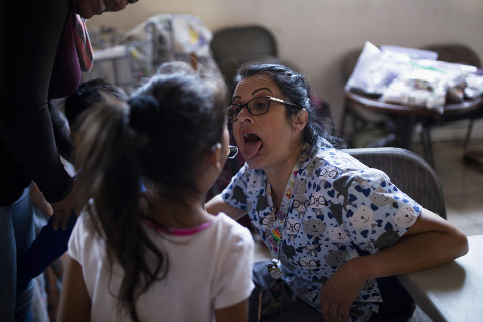In this Oct. 26, 2019, photo, pediatrician Paulina Avendano jokes with a girl as she asks her to open her mouth wide during an examination at a shelter for migrants in Tijuana, Mexico. The health crisis spans both sides of the border. In the past year, at least three children, detained by U.S. Border Patrol agents, have died from the flu while being held. They include a 16-year-old boy who was seen on security footage writhing in agony on the floor in a U.S. Border Patrol holding cell. (AP Photo/Gregory Bull)