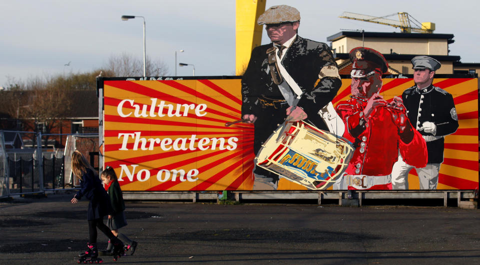 Children walks past a Loyalist mural in East Belfast a predominantly loyalist area in Belfast, Northern Ireland, Friday, March 24, 2017. Almost 20 years on from the Good Friday peace accord, which brought about the end of Northern Ireland's sectarian conflict, the city of Belfast has changed dramatically. Reminders of the past are everywhere _ murals and memorials to those killed in the conflict, along with peace walls that separate predominantly Protestant neighborhoods from mostly Catholic ones _ but there are also new shopping malls and cafes, new tech industries, and lots of tourists. (AP Photo/Peter Morrison)