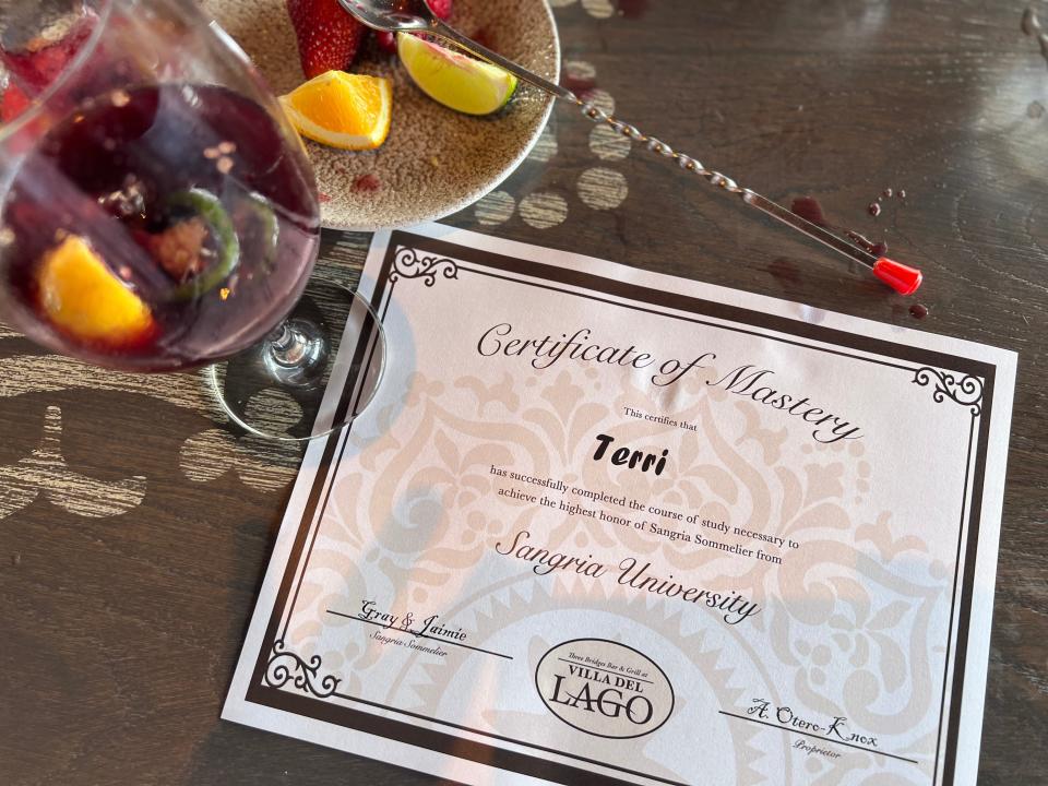 Certificate of mastery addressed to author on table next to glass of dark red sangria.