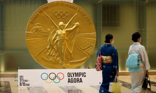 Women walk past a large-scale reproduction of Tokyo 2020 Olympic Games medal