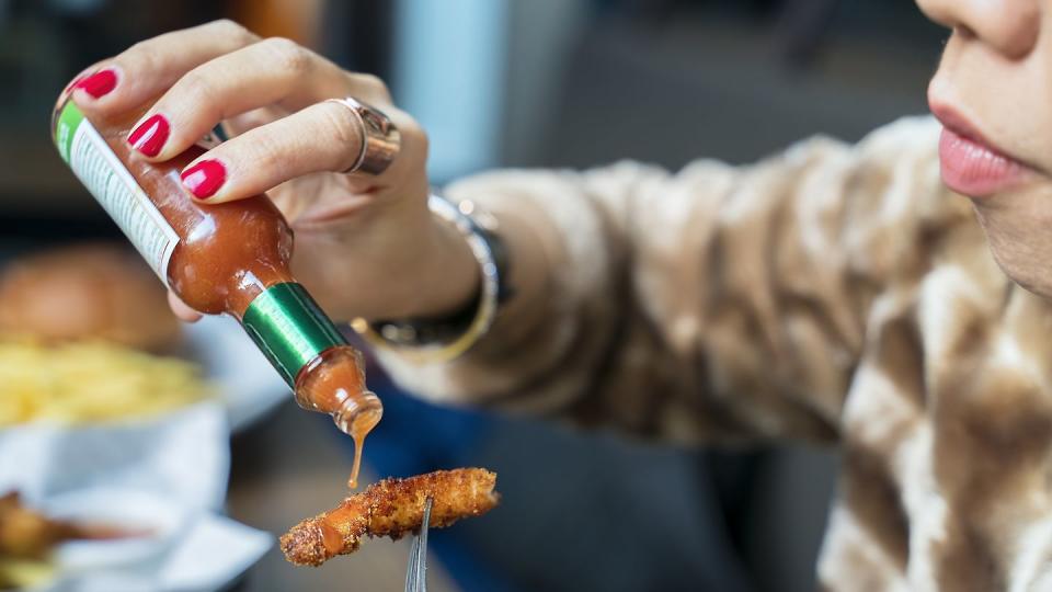 woman adding hot sauces on crispy, crunchy fried chicken fast food