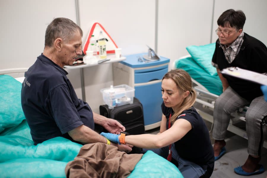 <em>A medical professional with the Polish Center for International Aid evaluates a Ukrainian patient transiting through the Medevac Hub in Rzeszów, Poland, while a family member looks on. (Courtesy Mariusz Ciszewski)</em>