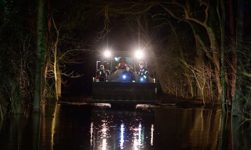 Volunteer firefighters are driven over a flooded road with a wheel loader not far from the Aller. The flood situation remains tense in many regions of Lower Saxony. Philipp Schulze/dpa