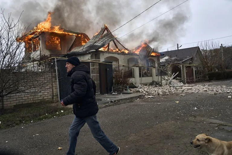 Un residente pasa junto a una casa en llamas tras un bombardeo ruso en Jersón, Ucrania, en la Nochebuena ortodoxa, el 6 de enero de 2023. (AP Foto/LIBKOS)