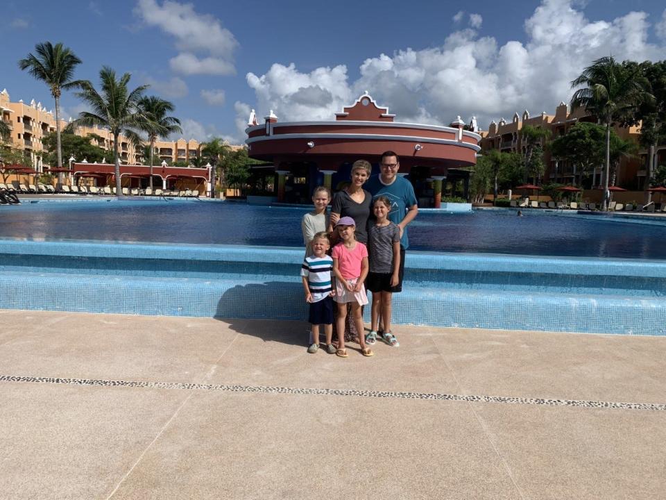 A family of six posing in front of a pool at a tropical resort.