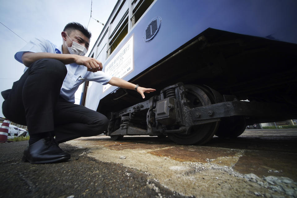 Yuta Azumi of the train planning division of Hiroshima Electric Railway Co., Ltd., explains a tram which survived the Hiroshima atomic bombing at a train maintenance facility in Hiroshima, western Japan, Monday, Aug. 3, 2020. It has been restored and repainted its original colors, will run on the street on Aug. 6 to commemorate the day of the U.S. first atomic bombing in the city. (AP Photo/Eugene Hoshiko)