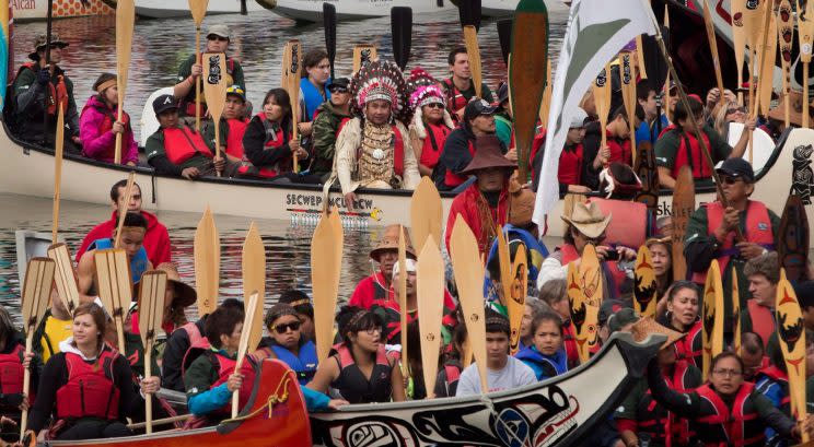 Rocky Mathias-Joe and Gerda Mathias, top centre in headdresses, of the Squamish First Nation, sit on a traditional canoe as paddles are raised on False Creek during an all nations canoe gathering held as part of 2013's Reconciliation Week in Vancouver, B.C. Photo from The Canadian Press