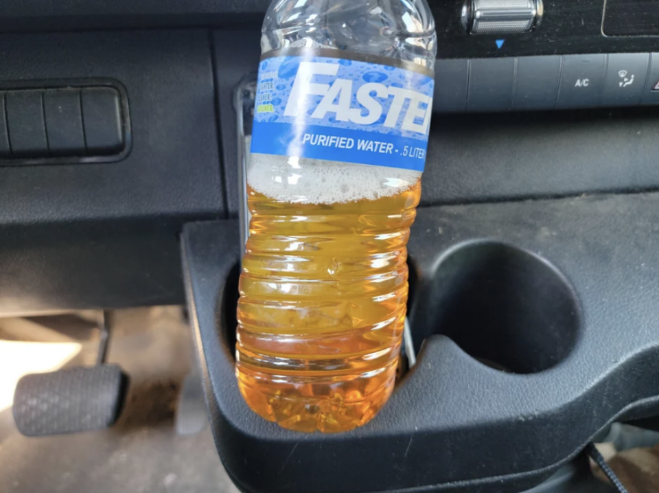 A plastic bottle with yellow liquid in it in the car's cupholder